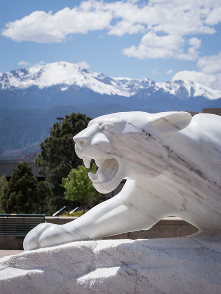 White mountain lion statue in front of mountains and trees