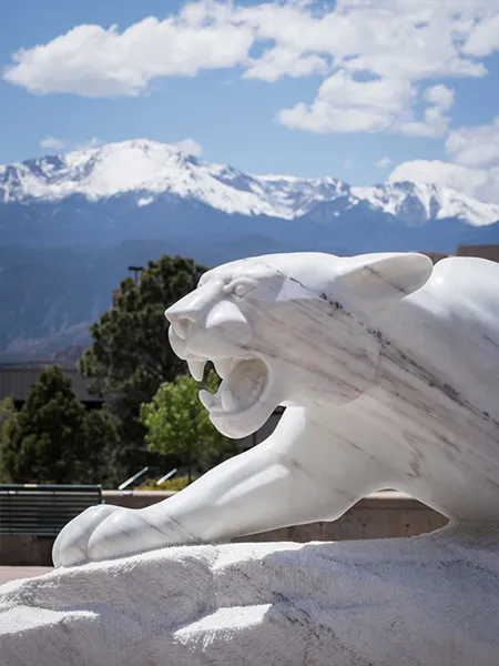 White mountain lion statue in front of mountains and trees